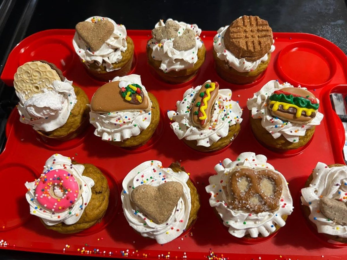 Tray of frosted apple pupcakes decorated with sprinkles and novelty biscuit toppers