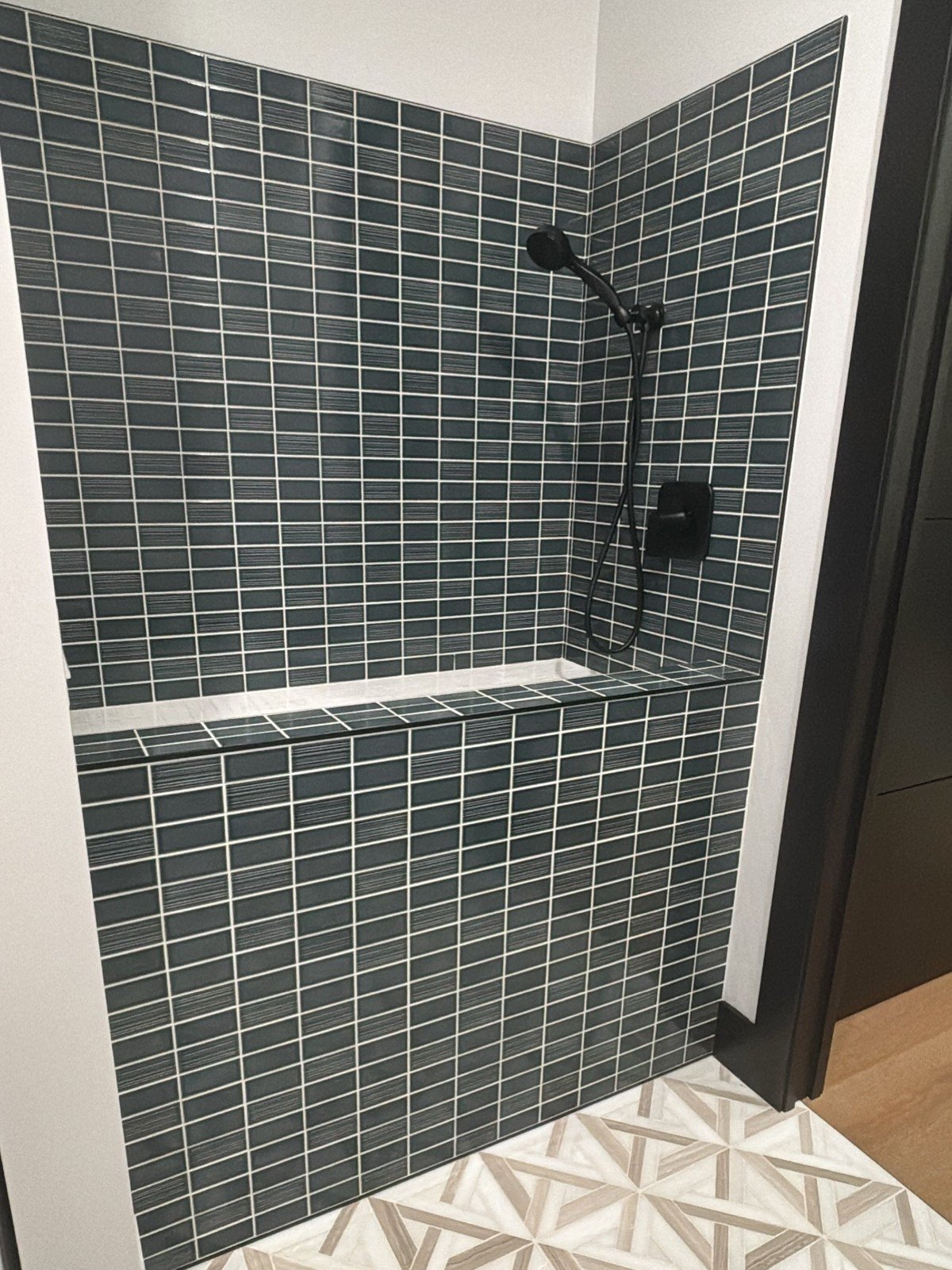 Newly completed dog wash station with dark teal-gray subway tile walls and matte black plumbing fixtures including a handheld showerhead. No text visible in the image. (Closest text-free match: dark tile rather than a pure black pan.)