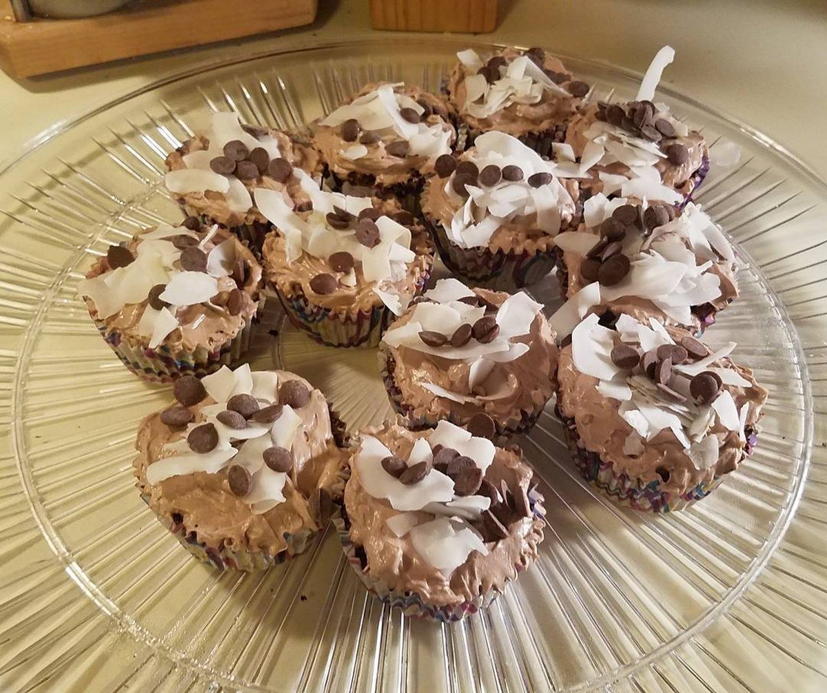 Carob pupcakes with tan frosting, carob chips, and coconut shavings on a glass plate