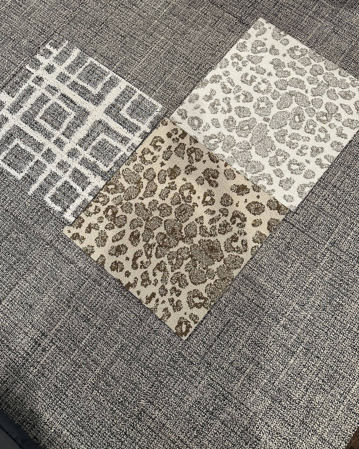 Top-down photo of carpet tile samples (geometric, leopard print, plain gray) layered on installed carpet tile floor. No readable text.