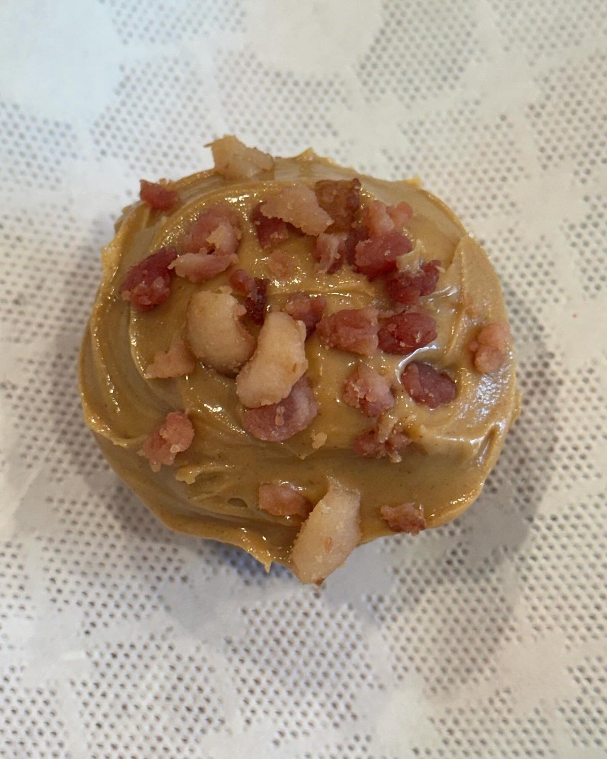 Close-up of a savory pupcake with tan frosting topped with bacon bits