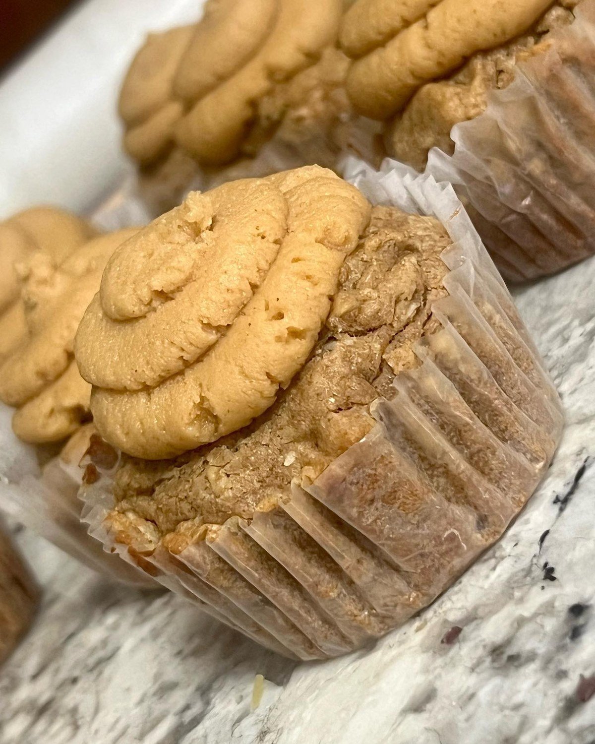 Close-up of homemade peanut butter banana pupcakes with swirled tan frosting in paper liners