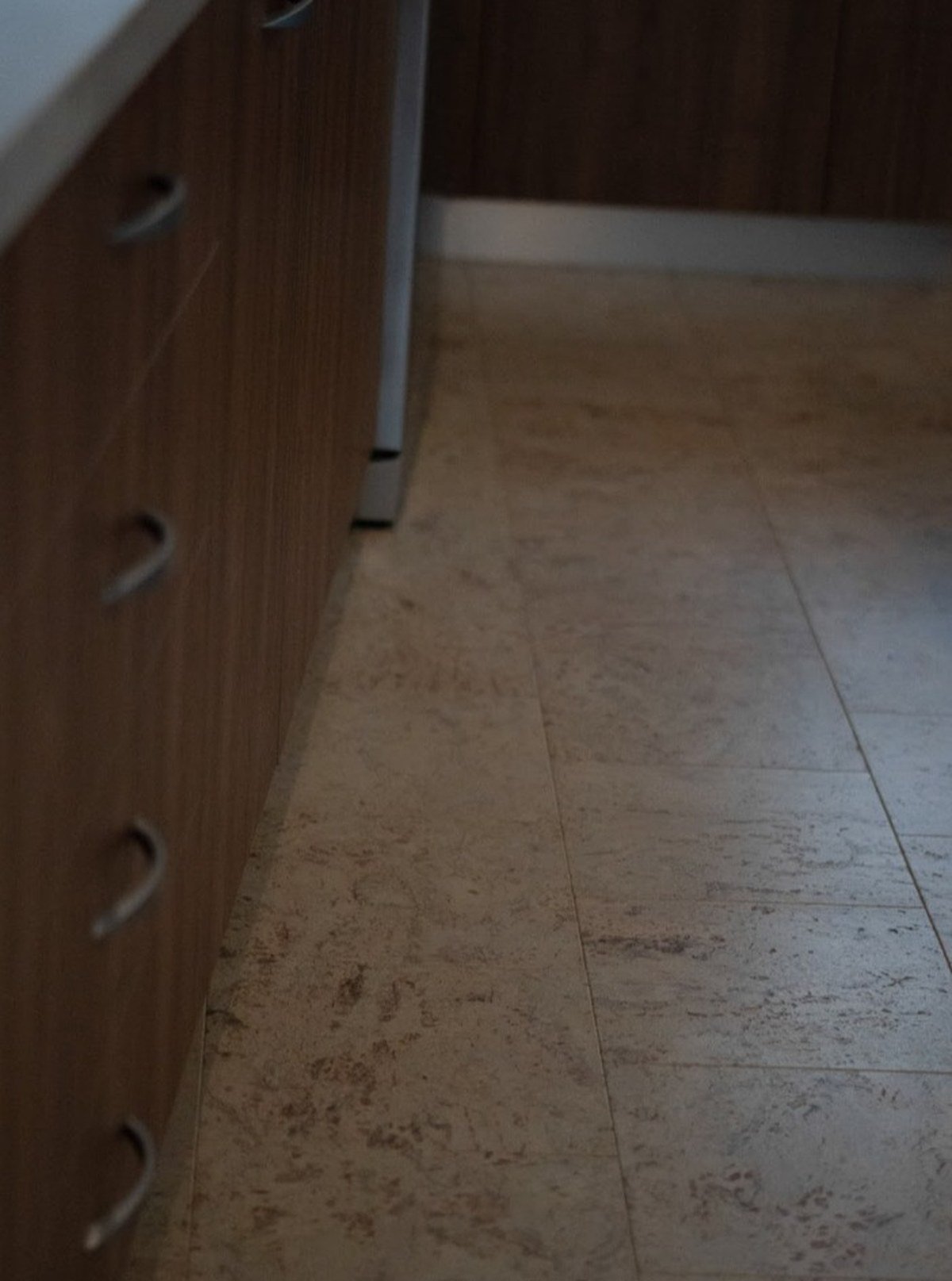 Low-angle close-up of beige cork tiles with brown veining beside dark wood kitchen cabinetry. No readable text.