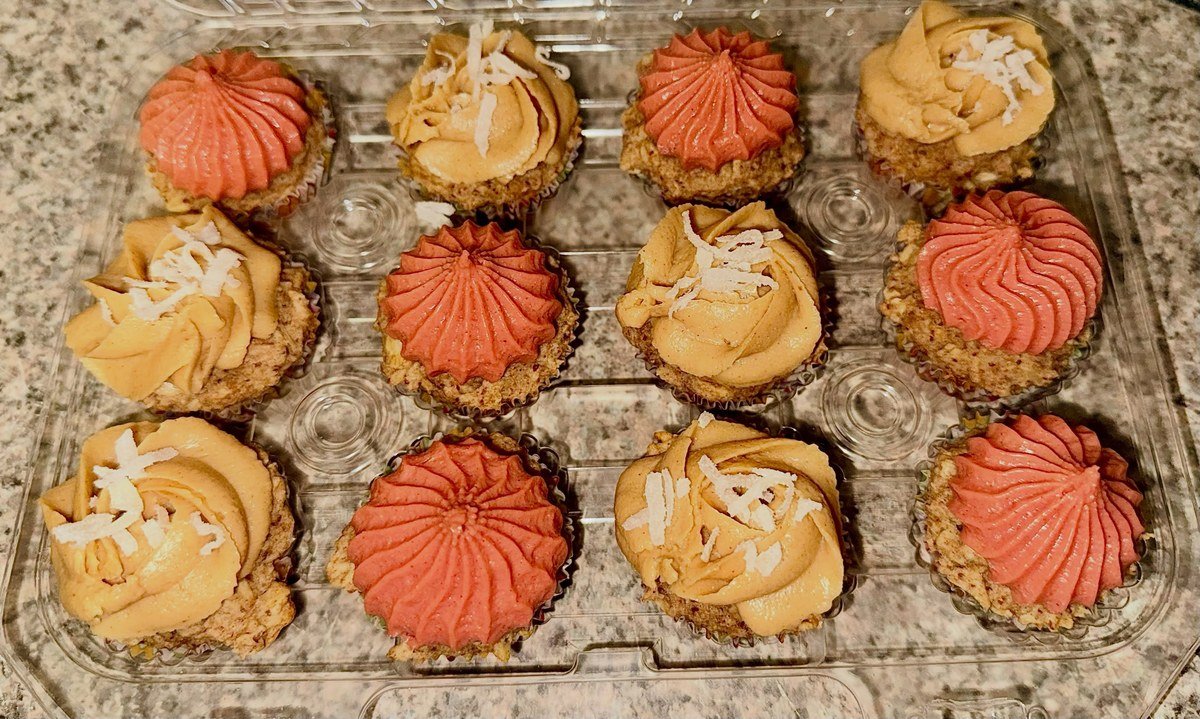 Oat pupcakes with pink swirled frosting and peanut butter frosting with coconut flakes in a bakery box