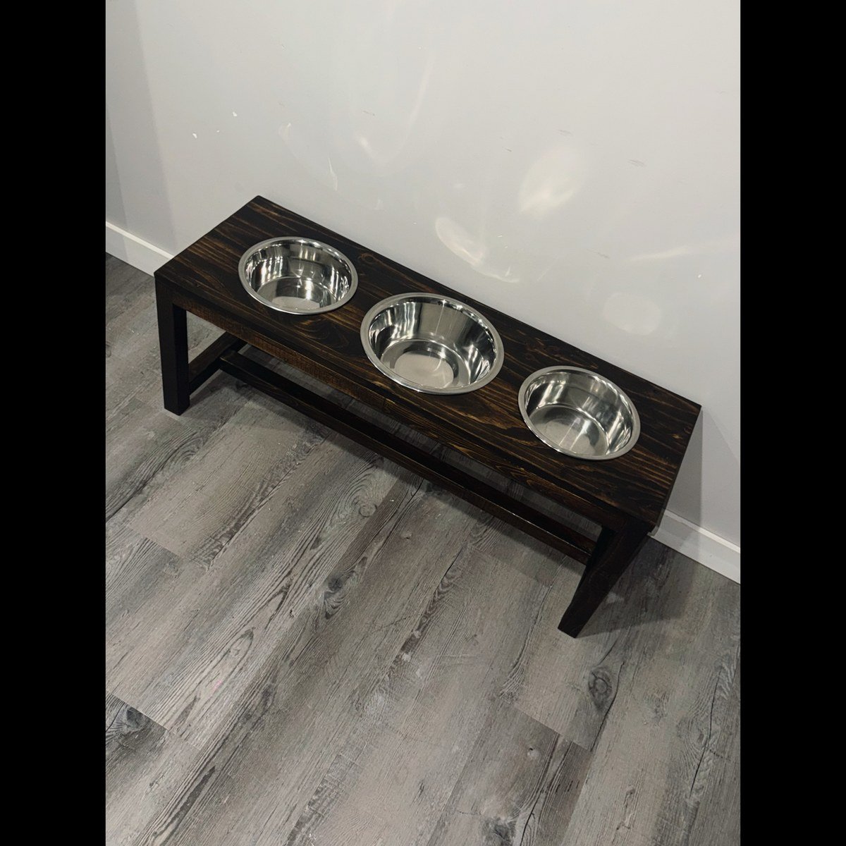 Custom-built farmhouse elevated feeder, dark-stained wood with three steel bowls inset in a row. No readable text.