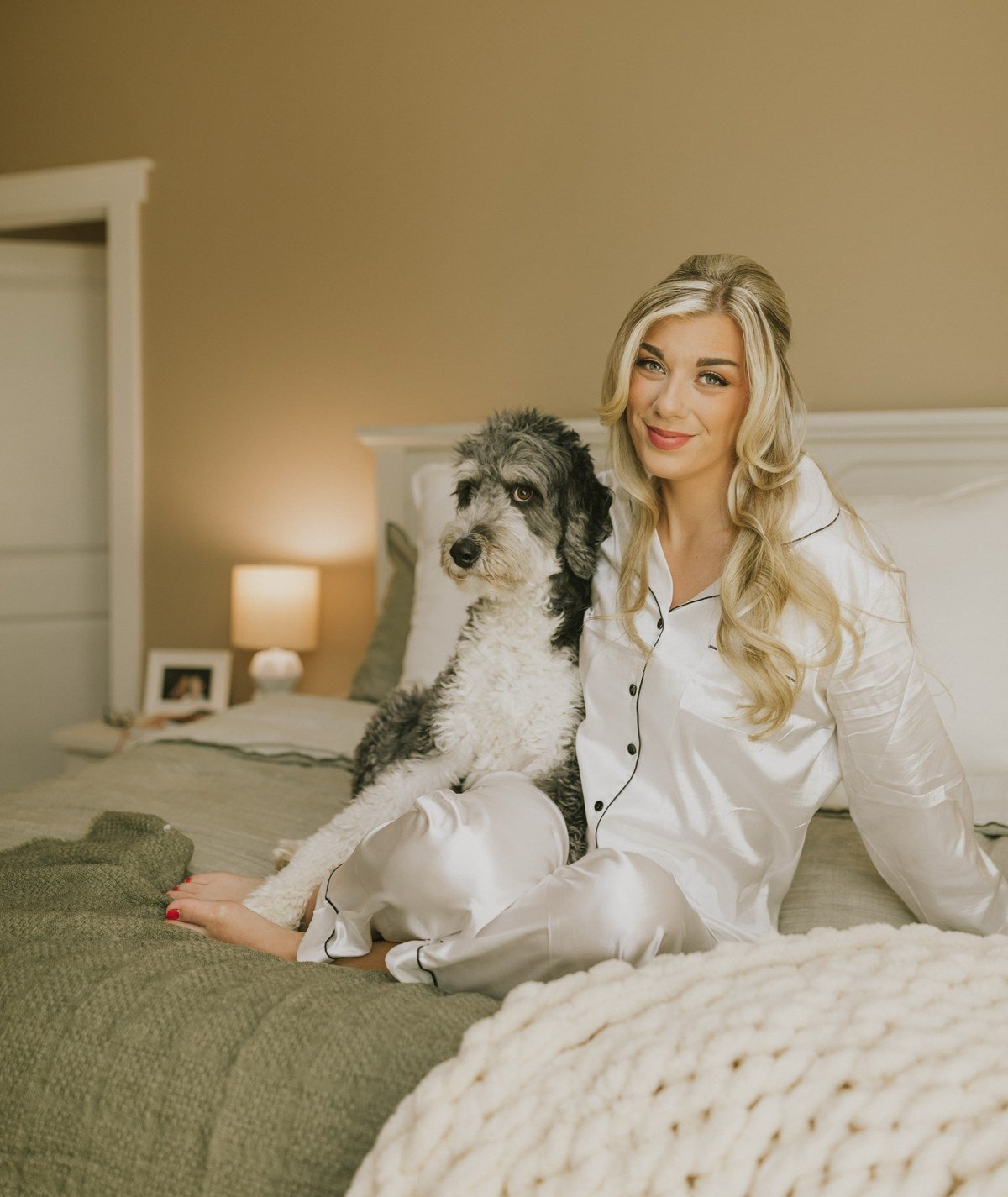 Bride in satin pajamas cuddling her dog on the bed on the wedding morning
