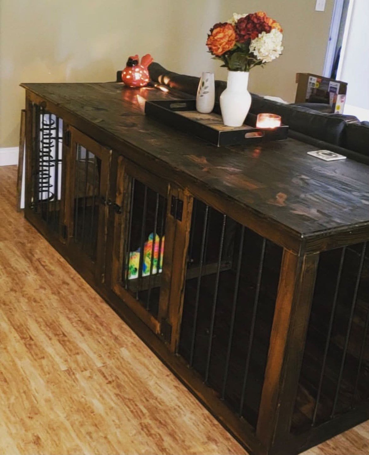 Large custom-built wooden dog kennel used as a console table, dark-stained wood with black metal bar fronts, styled top. No readable text.