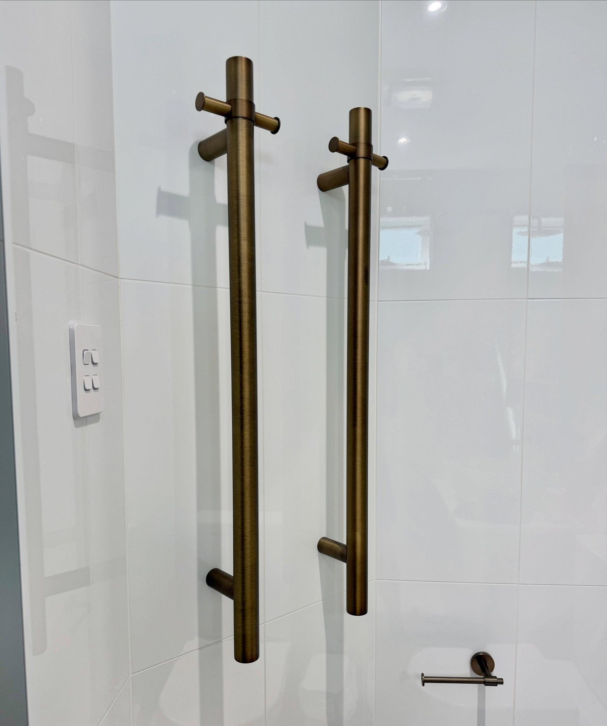 Clean modern bathroom with two brushed-bronze vertical heated towel rails mounted on glossy white tile. No readable text.
