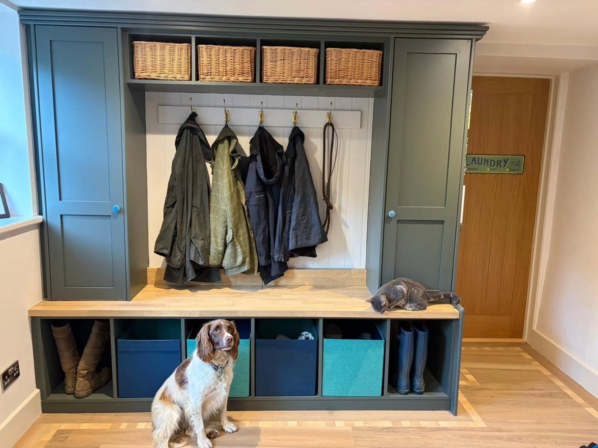 Brown-and-white spaniel in a custom boot room/mudroom with dark green cabinetry and boots by the bench.