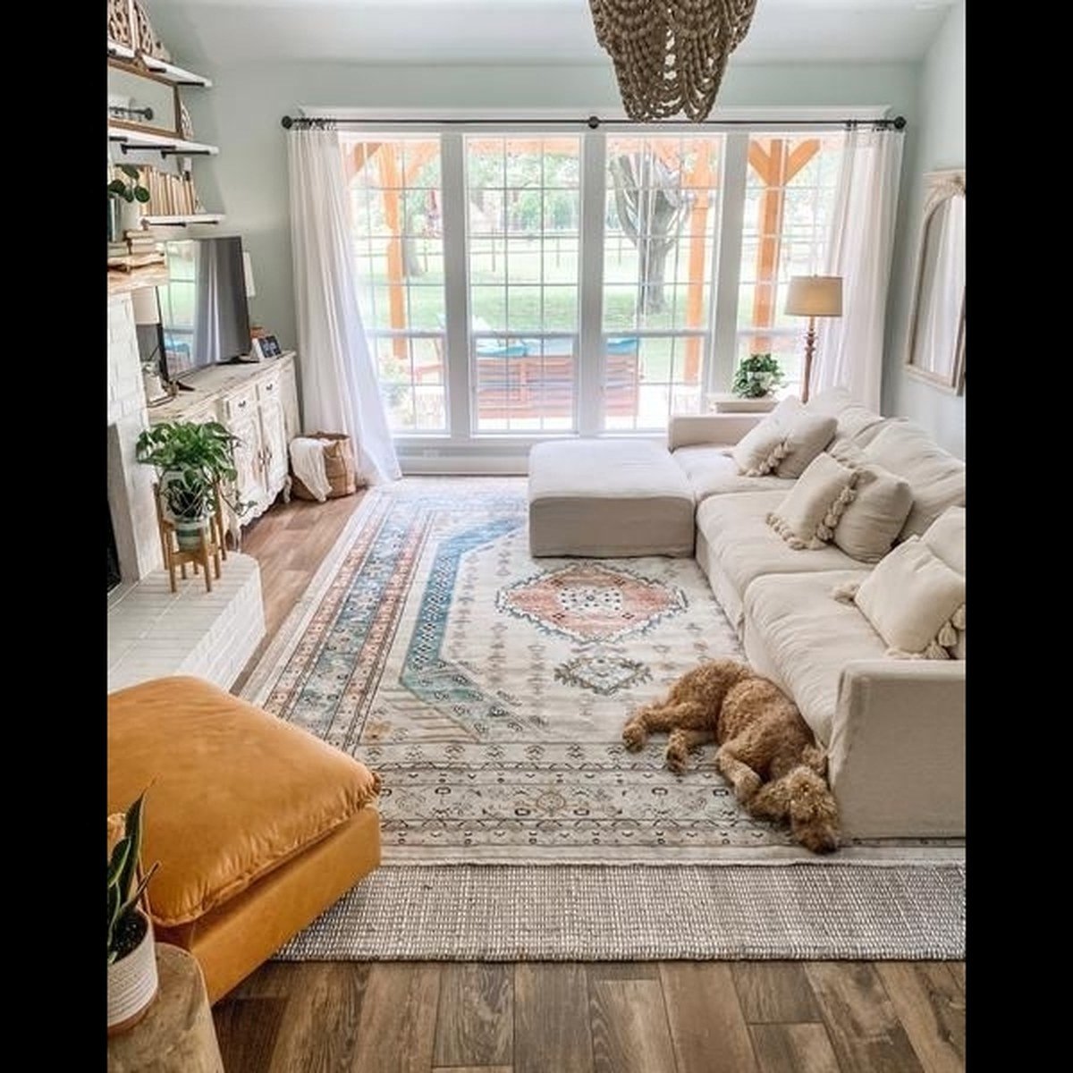 Curly-haired brown dog asleep on a patterned vintage-style rug layered over a neutral woven rug in a bright living room.