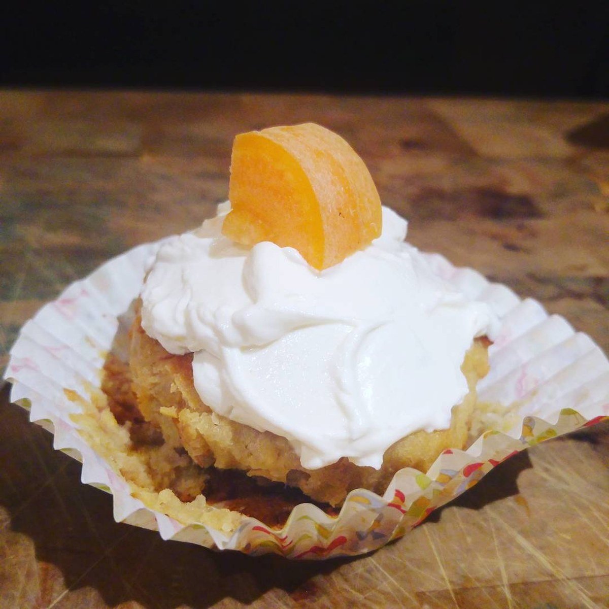 Pupcake with white frosting and a carrot slice topper in a patterned liner