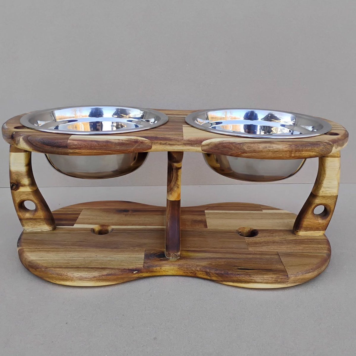 Handmade acacia wood elevated feeder with two steel bowls, plain backdrop. Text-free stand-in for the nameplate concept.
