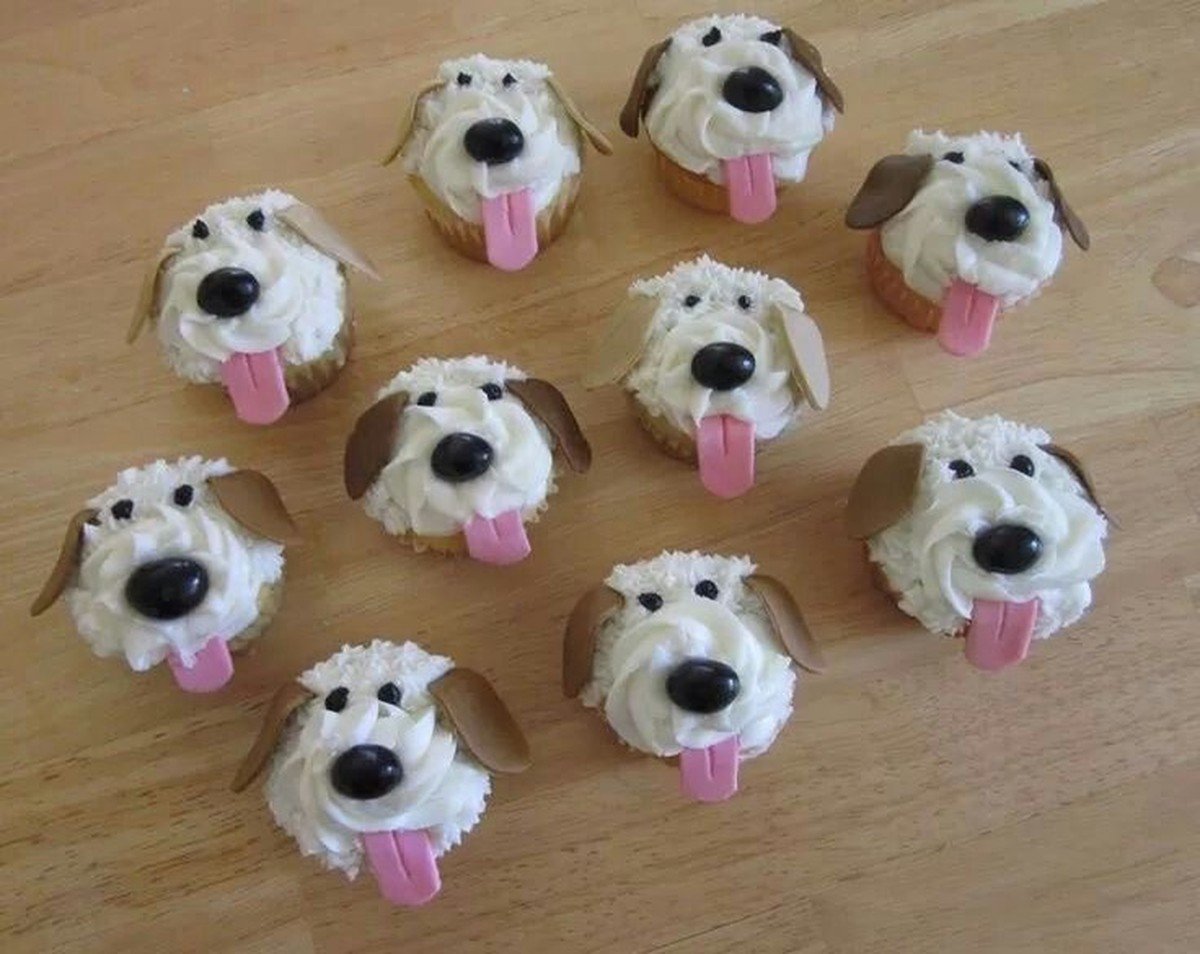 Eleven cupcakes frosted as fluffy white dog faces with fondant ears, noses, and pink tongues.