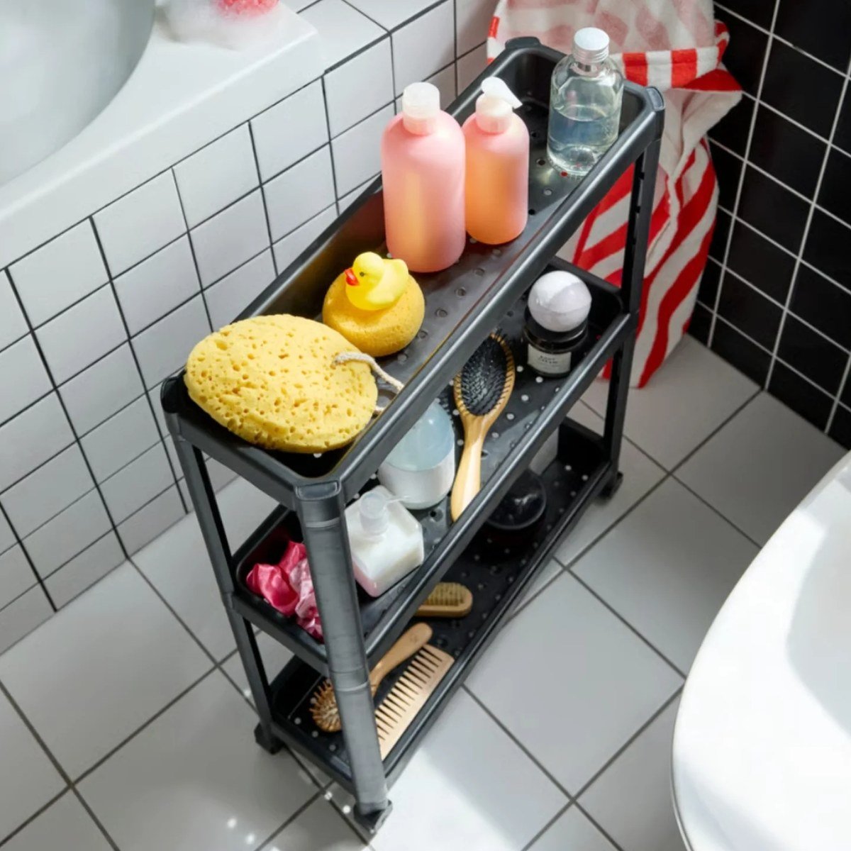 Black three-shelf rolling storage cart stocked with bath supplies in a home bathroom.