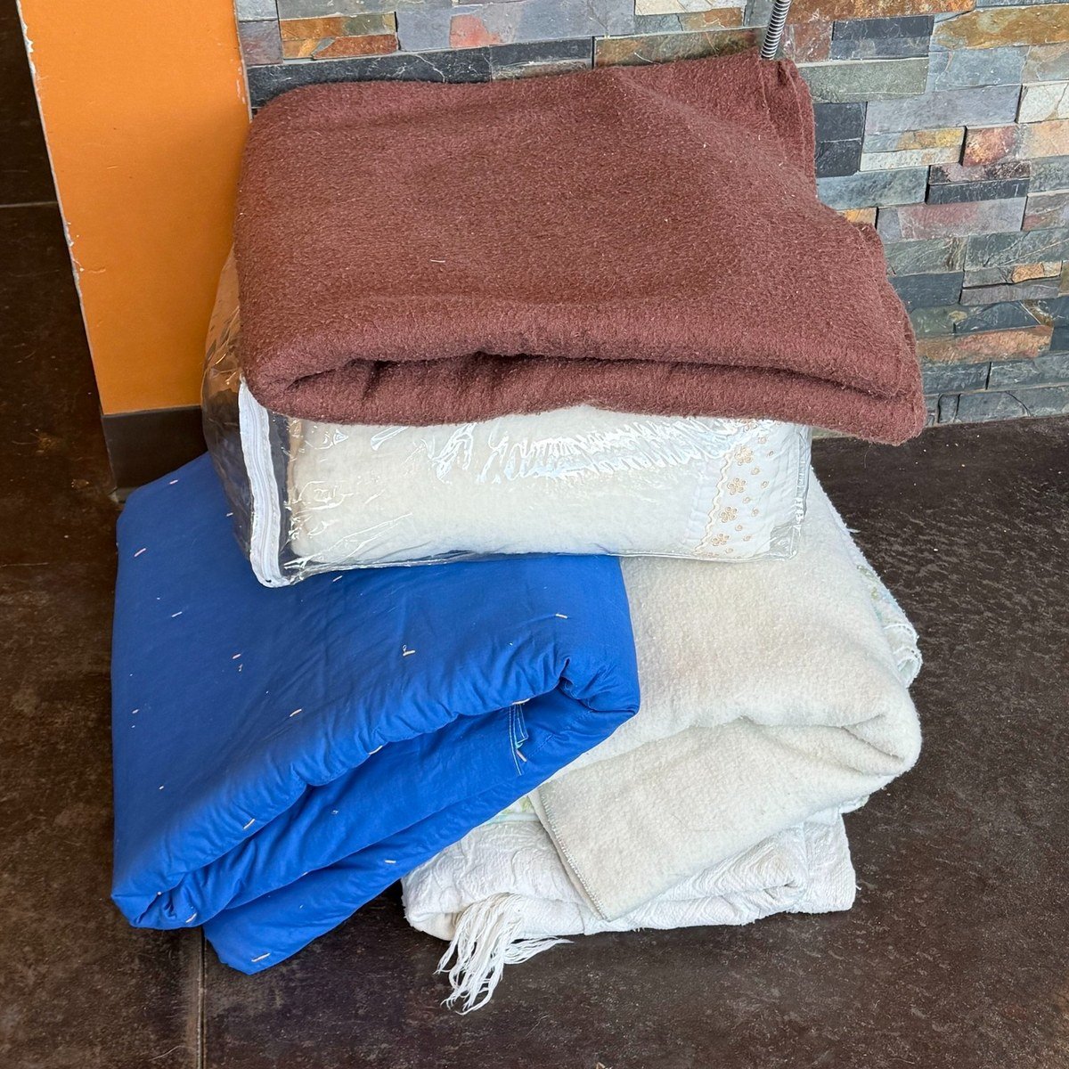 Stack of folded donated blankets (brown, white, blue, cream) on a floor; no readable text