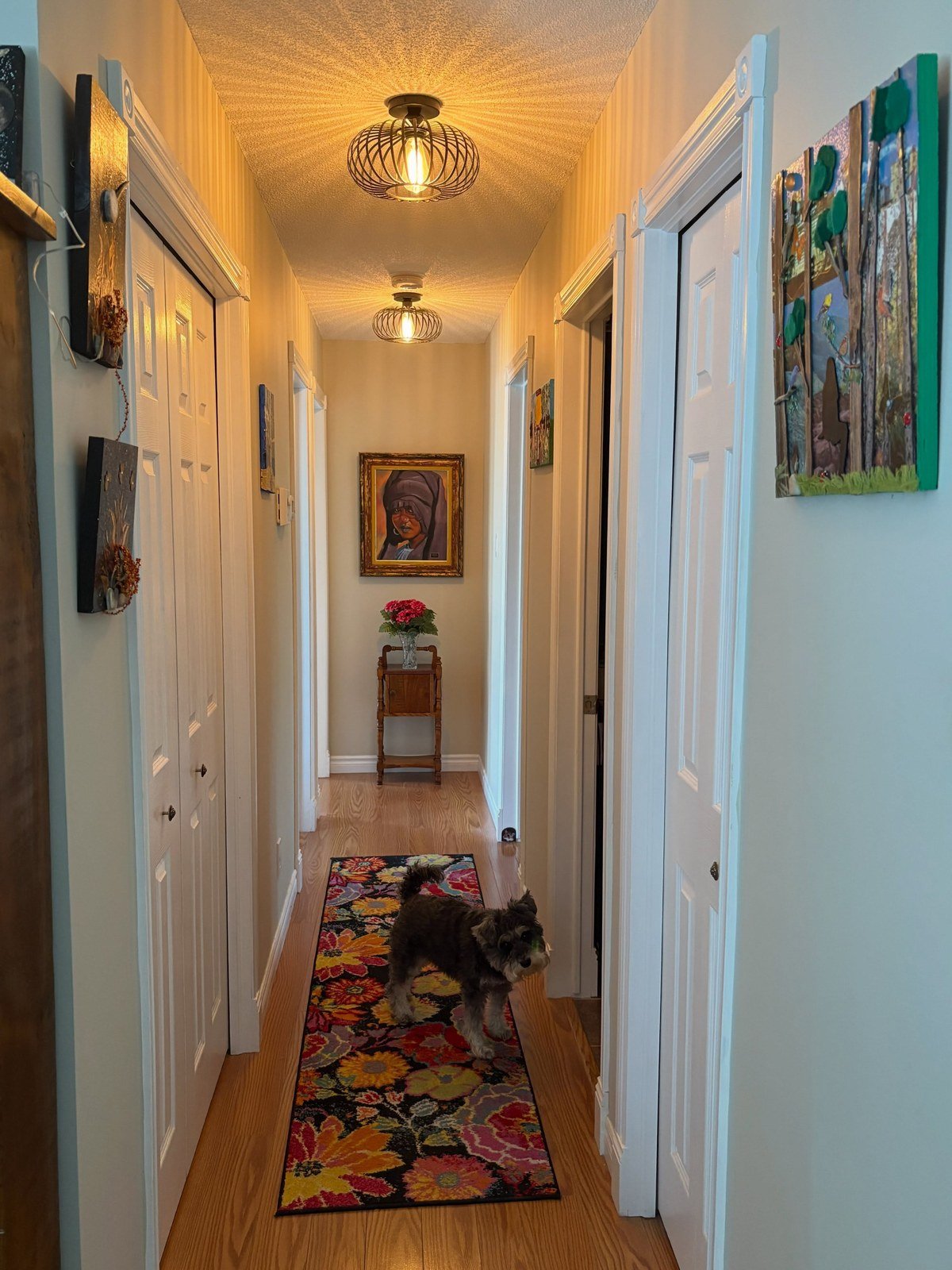 Long narrow hallway with a colorful floral runner; small terrier standing on the rug.