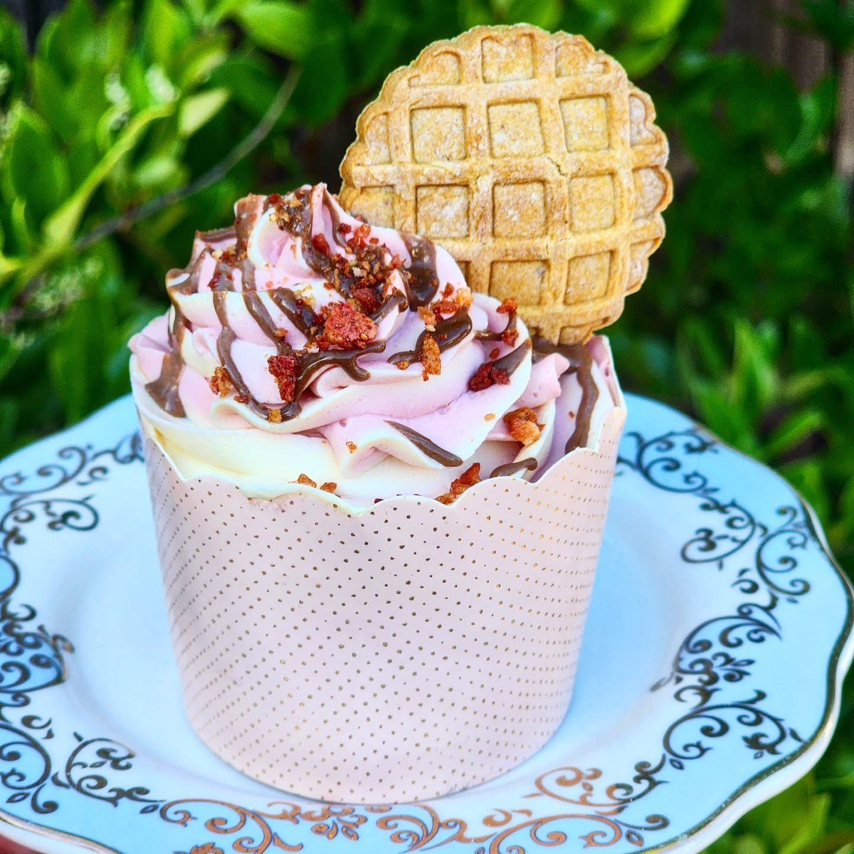 Strawberry pupcake with pink yogurt frosting, carob drizzle, strawberry pieces, and a waffle cookie