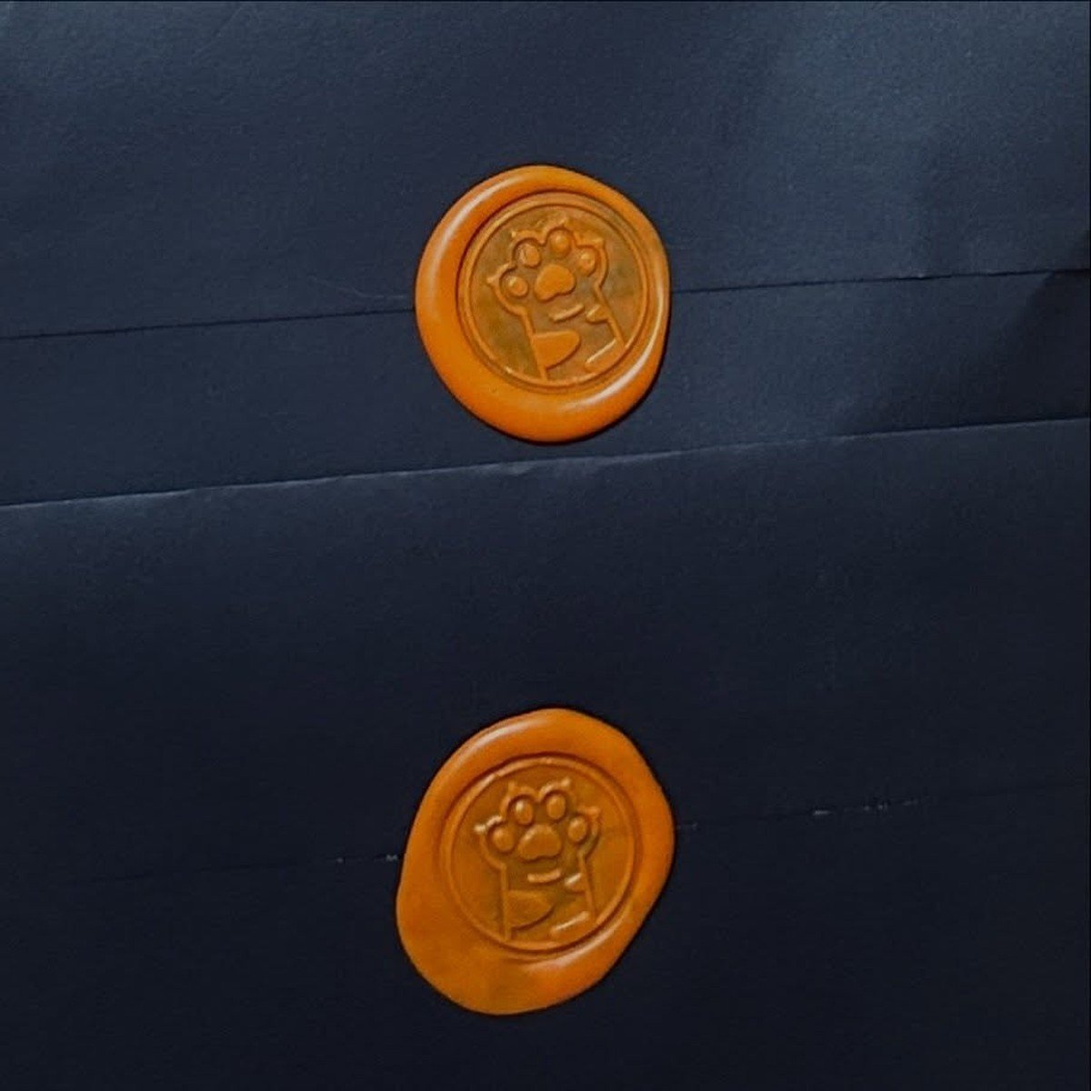 Two dark envelopes sealed with orange wax stamps embossed with a paw logo.