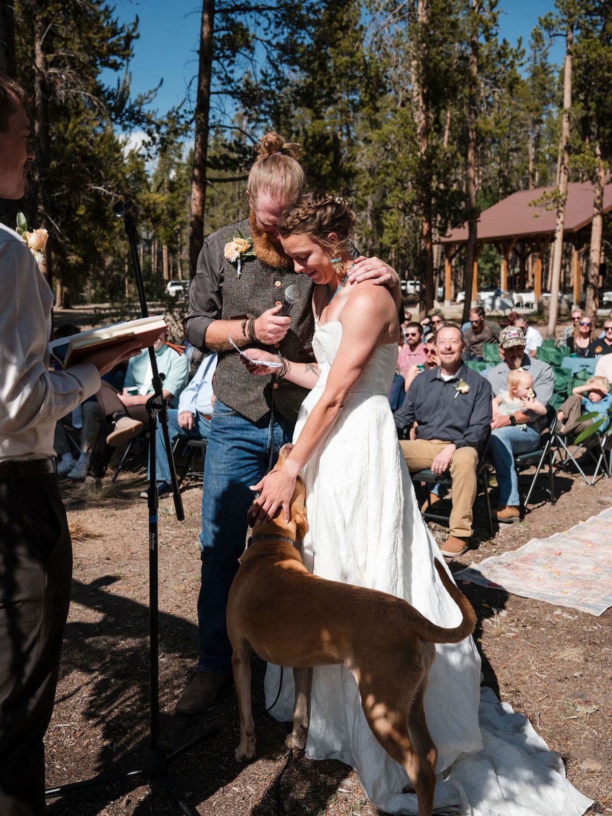 Couple exchanging vows outdoors with their brown dog standing beside the bride
